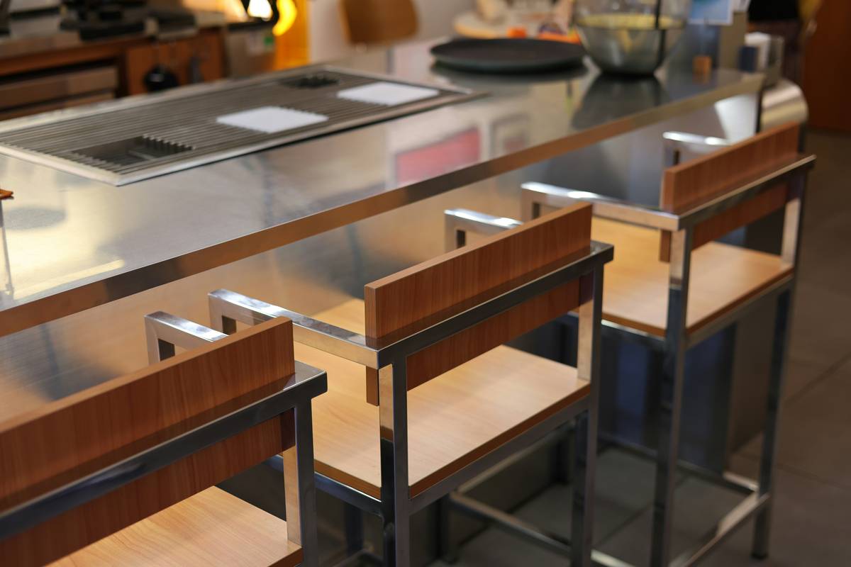 Three simple wooden bar stools lined up beside a kitchen island with natural lighting highlighting grain texture